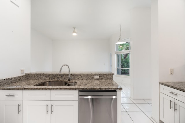 kitchen featuring stainless steel dishwasher, dark stone countertops, a sink, and white cabinetry