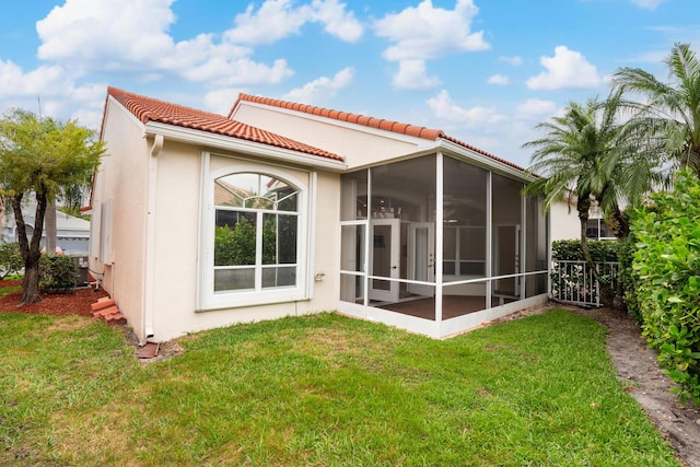 back of property featuring a sunroom, a tile roof, stucco siding, and a yard