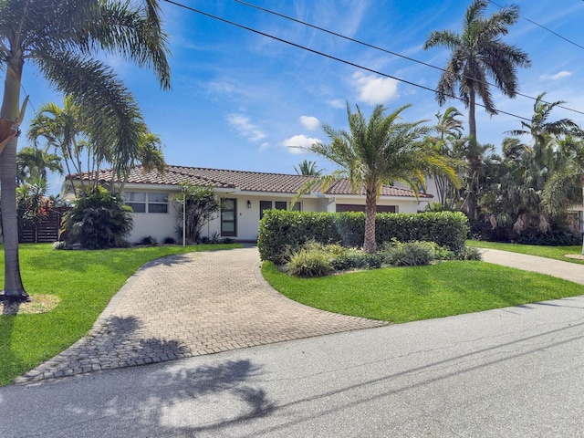 view of front facade featuring a tiled roof, a front lawn, stucco siding, and decorative driveway