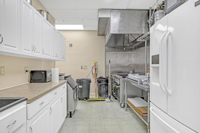 kitchen featuring white cabinets, white refrigerator with ice dispenser, and a drop ceiling