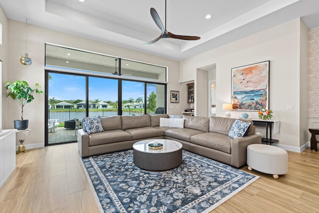 living area featuring light wood-style floors, baseboards, a tray ceiling, and a ceiling fan