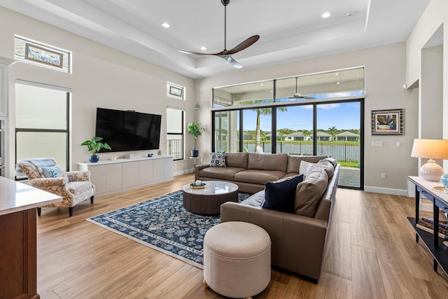 living room with light wood-type flooring, ceiling fan, and a tray ceiling