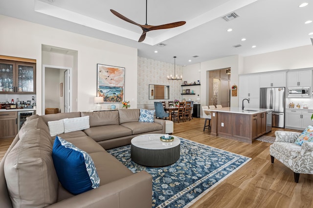 living area featuring a tray ceiling, recessed lighting, beverage cooler, light wood-type flooring, and bar area