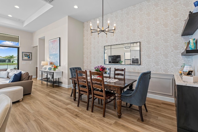 dining space with wallpapered walls, a notable chandelier, and light wood-style floors