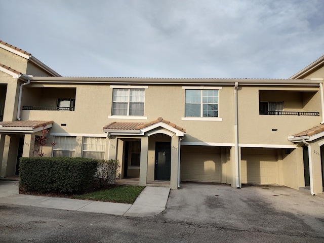 multi unit property featuring a garage, driveway, a tiled roof, and stucco siding