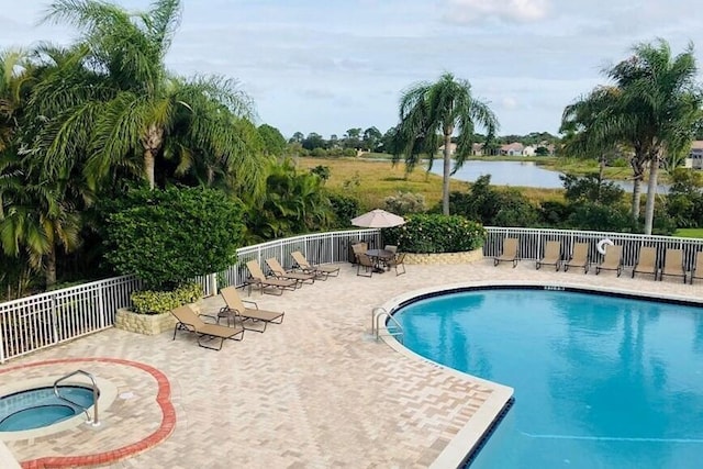 pool featuring a community hot tub, a patio area, a water view, and fence