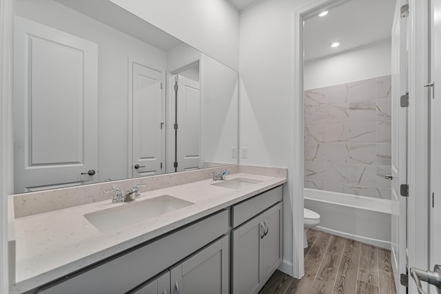 full bathroom with hardwood / wood-style flooring, vanity, tiled shower / bath combo, and toilet