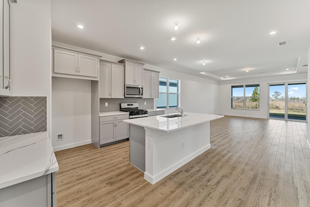 kitchen featuring sink, gray cabinets, an island with sink, stainless steel appliances, and light stone countertops