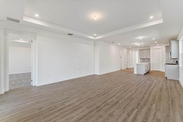 unfurnished living room featuring a tray ceiling and light hardwood / wood-style floors