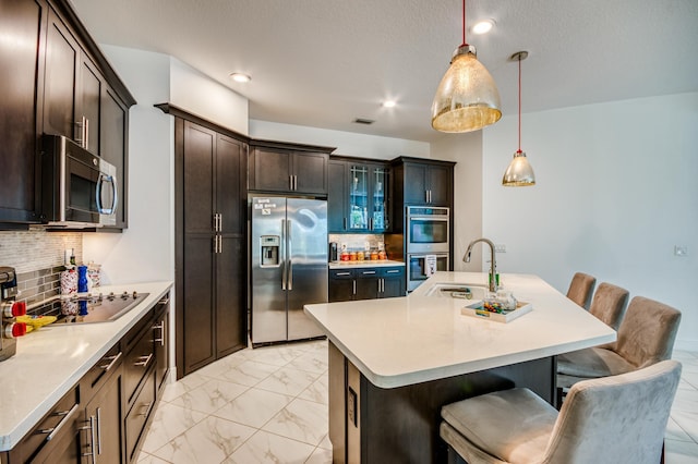 kitchen featuring a kitchen island with sink, stainless steel appliances, sink, a kitchen bar, and pendant lighting