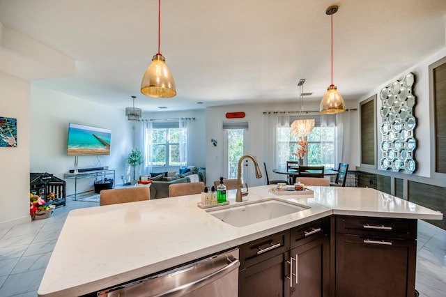 kitchen featuring an island with sink, hanging light fixtures, dark brown cabinetry, sink, and stainless steel dishwasher