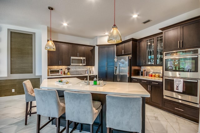 kitchen featuring an island with sink, appliances with stainless steel finishes, dark brown cabinetry, and pendant lighting