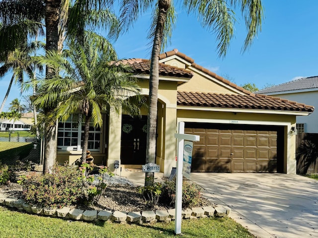 mediterranean / spanish-style house featuring a tile roof, stucco siding, fence, a garage, and driveway