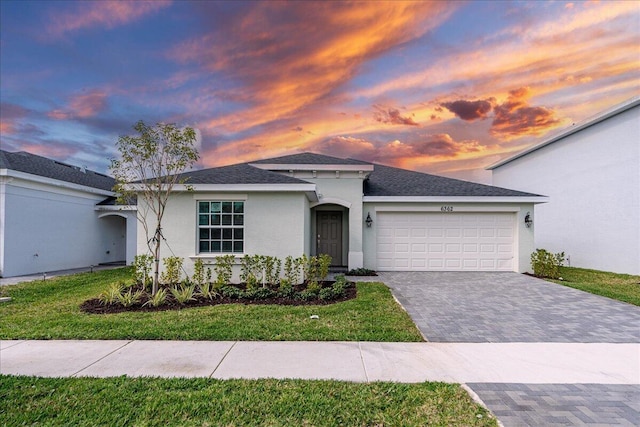 single story home featuring a garage, a shingled roof, decorative driveway, a lawn, and stucco siding