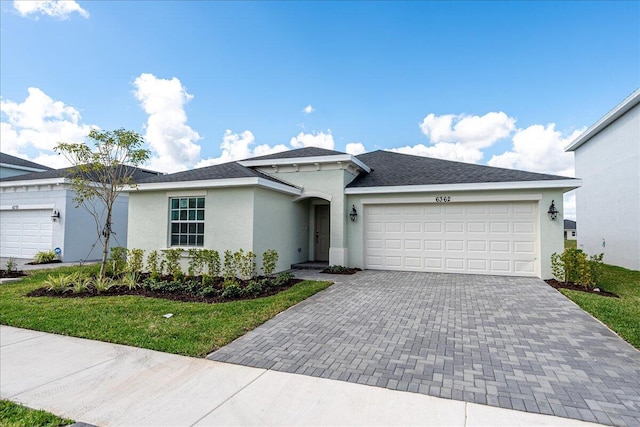 single story home with an attached garage, a front yard, decorative driveway, and stucco siding