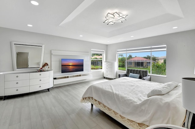 bedroom with light hardwood / wood-style flooring and a tray ceiling