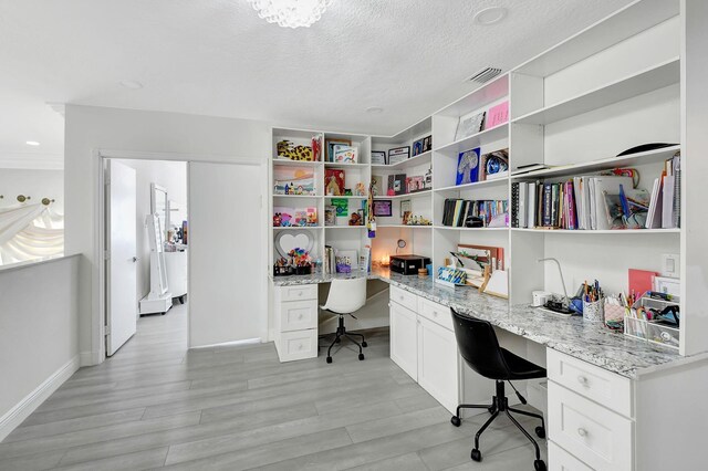 office featuring built in desk, a textured ceiling, and light hardwood / wood-style floors