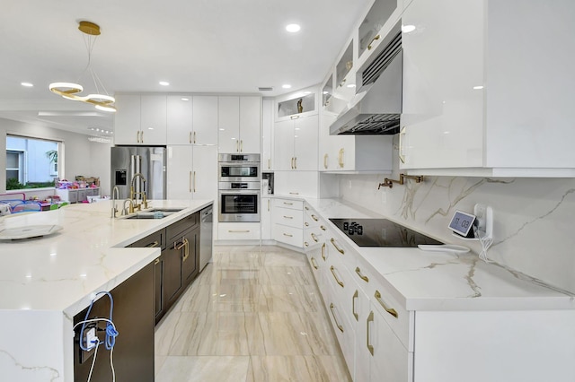 kitchen featuring white cabinetry, light stone counters, hanging light fixtures, appliances with stainless steel finishes, and wall chimney range hood