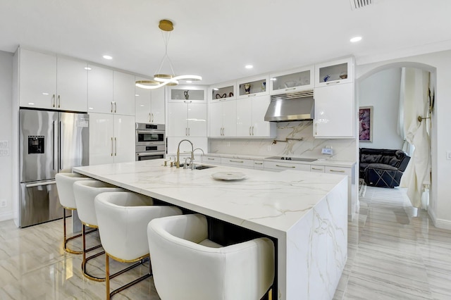 kitchen featuring white cabinets, exhaust hood, an island with sink, and appliances with stainless steel finishes