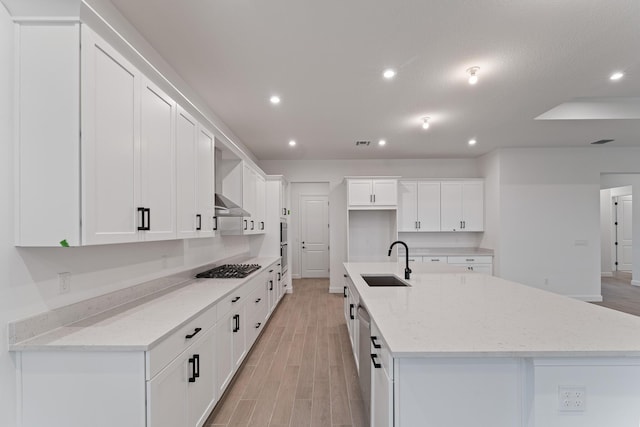 kitchen with a spacious island, white cabinetry, sink, and light stone counters