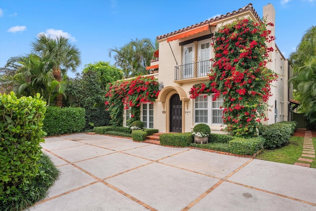 mediterranean / spanish home featuring a balcony, a tile roof, and stucco siding