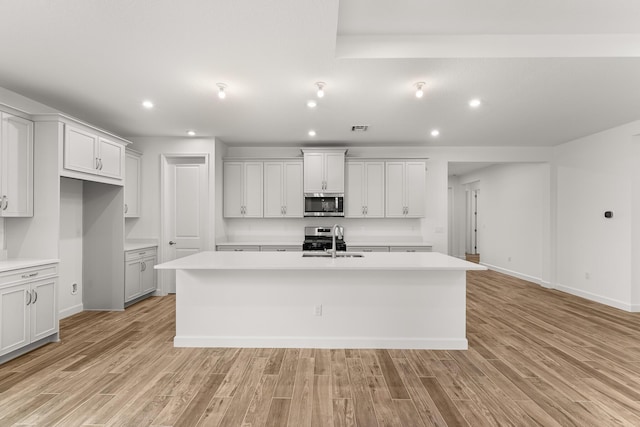 kitchen featuring an island with sink, a sink, stainless steel appliances, light countertops, and light wood-type flooring