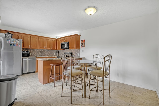 kitchen with a breakfast bar, brown cabinets, tasteful backsplash, light countertops, and appliances with stainless steel finishes