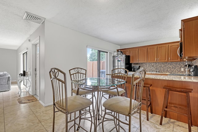 dining room featuring a textured ceiling, light tile patterned flooring, visible vents, and baseboards