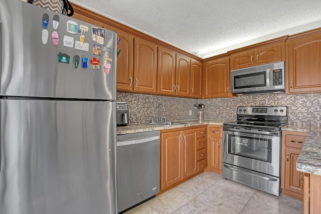 kitchen featuring a textured ceiling, appliances with stainless steel finishes, a sink, and light stone counters