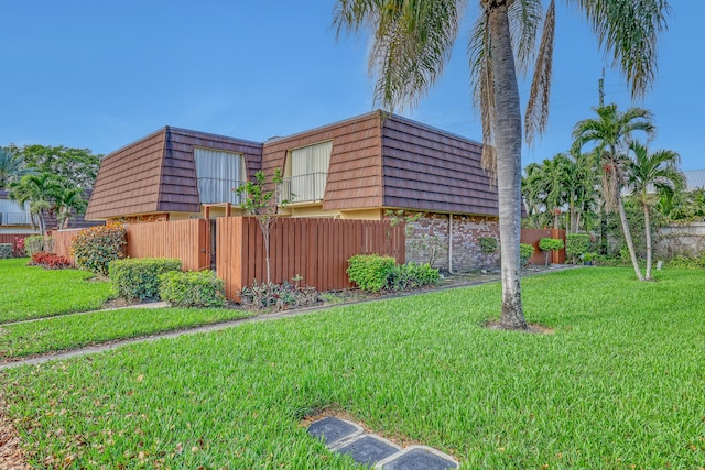 view of side of home featuring fence, a lawn, and mansard roof