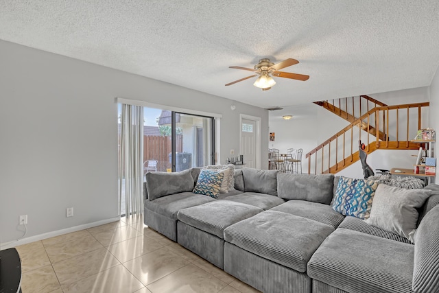 living area featuring light tile patterned floors, baseboards, ceiling fan, stairs, and a textured ceiling