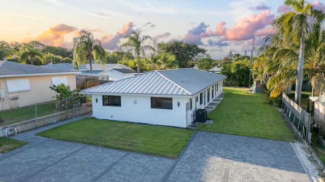 back of property at dusk featuring fence, metal roof, a lawn, and stucco siding