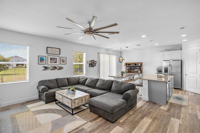 living area with recessed lighting, light wood-style flooring, a textured ceiling, and baseboards