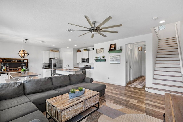 living room with stairway, light wood-style floors, visible vents, and a textured ceiling