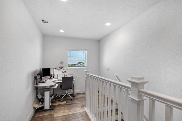 home office featuring wood finished floors, visible vents, baseboards, a textured ceiling, and a textured wall