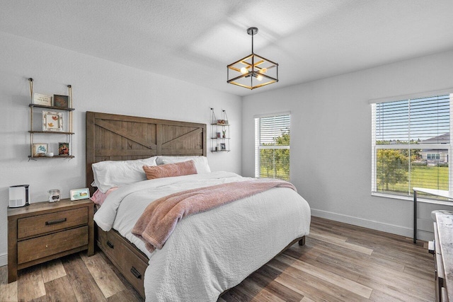 bedroom featuring a notable chandelier, wood finished floors, baseboards, and a textured ceiling