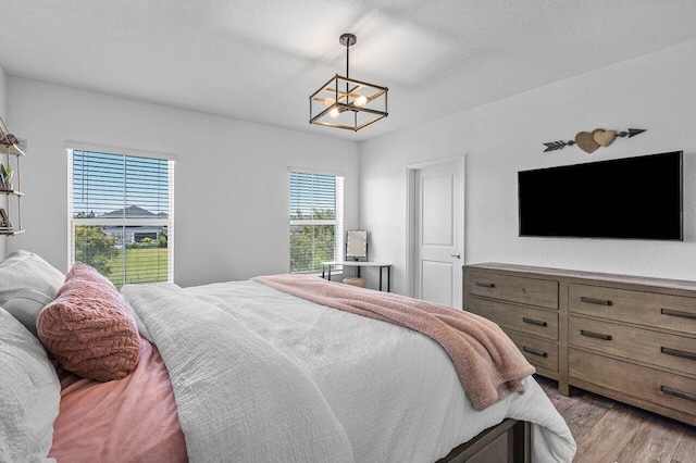 bedroom featuring light wood-style flooring, a textured ceiling, and an inviting chandelier