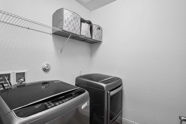 washroom with laundry area, a textured wall, and washing machine and clothes dryer