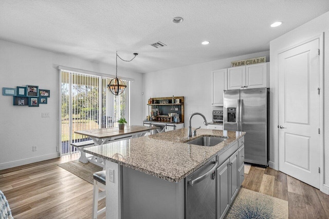 kitchen with visible vents, a sink, stainless steel appliances, light wood-style floors, and light stone countertops