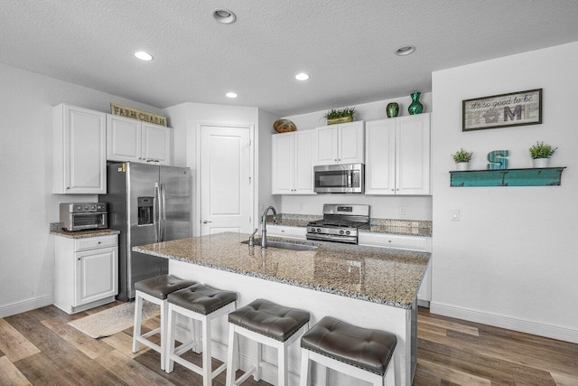 kitchen featuring a sink, dark stone countertops, dark wood-style floors, stainless steel appliances, and a breakfast bar area