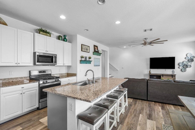 kitchen with visible vents, a sink, light stone counters, dark wood finished floors, and stainless steel appliances