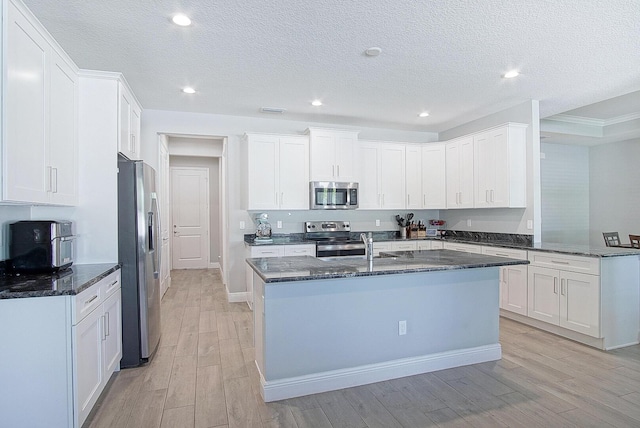 kitchen with sink, white cabinetry, stainless steel appliances, dark stone counters, and light wood-type flooring