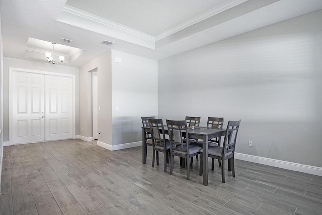 dining space with an inviting chandelier, ornamental molding, wood-type flooring, and a tray ceiling