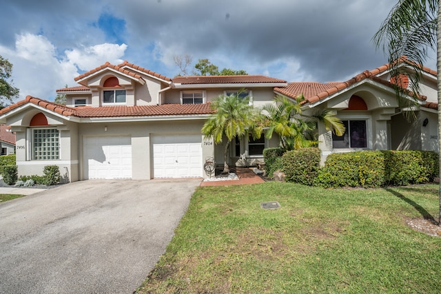 mediterranean / spanish house featuring driveway, a tiled roof, an attached garage, a front lawn, and stucco siding