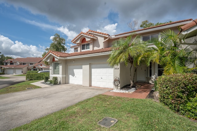 mediterranean / spanish house featuring aphalt driveway, stucco siding, an attached garage, a tiled roof, and a front lawn