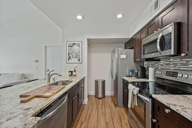 kitchen featuring sink, appliances with stainless steel finishes, dark brown cabinets, light stone countertops, and light hardwood / wood-style floors