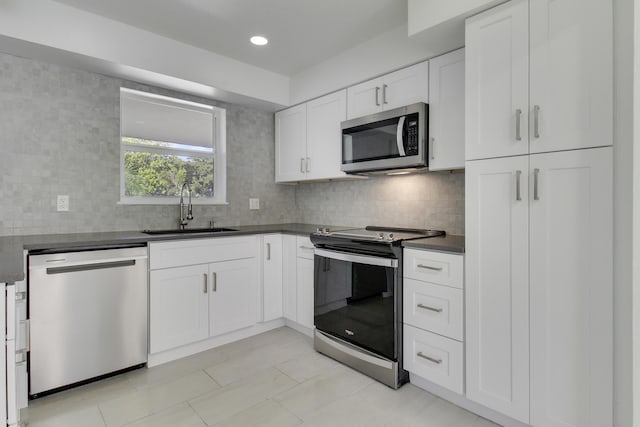 kitchen featuring stainless steel appliances, a sink, white cabinetry, tasteful backsplash, and dark countertops