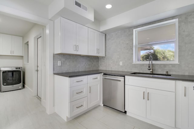 kitchen featuring white cabinets, dark countertops, washer / clothes dryer, stainless steel dishwasher, and a sink