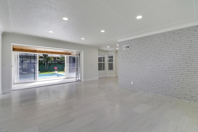 empty room featuring a textured ceiling, recessed lighting, brick wall, visible vents, and baseboards