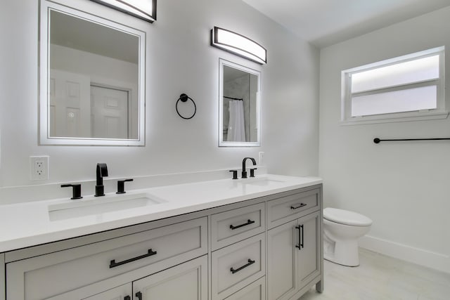 bathroom featuring double vanity, a sink, toilet, and baseboards